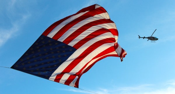 Honor depicted with the American flag flying against a blue sky background with a helicopter.