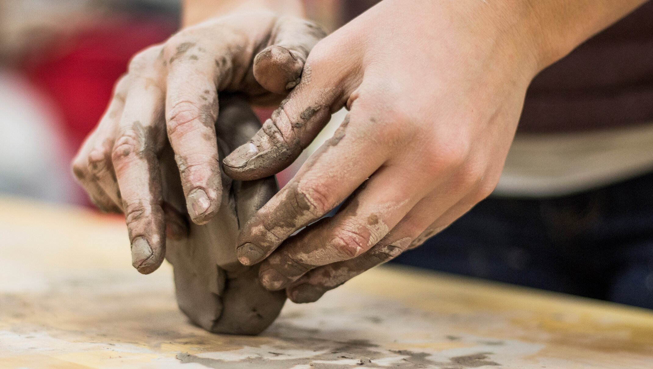Excellence requires much practice. This is depicted by a two hands forming a piece of potter's clay.