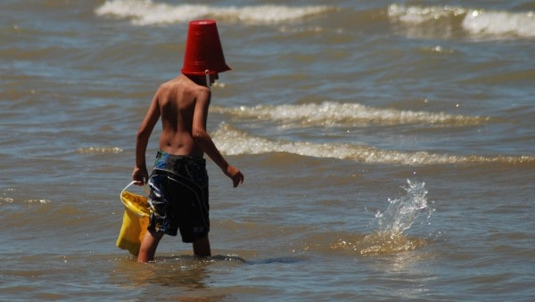 Planning for success is like planning for vacation, depicted by boy wearing a sand pail on head and carrying one as walking into the ocean.