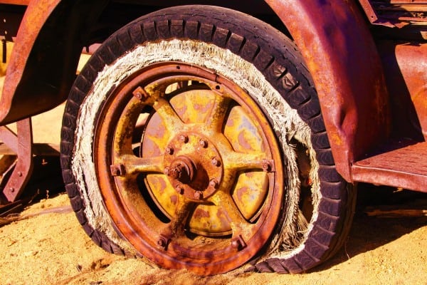 Owning the flaws of business depicted by a flat tire on a rusted out old vehicle.