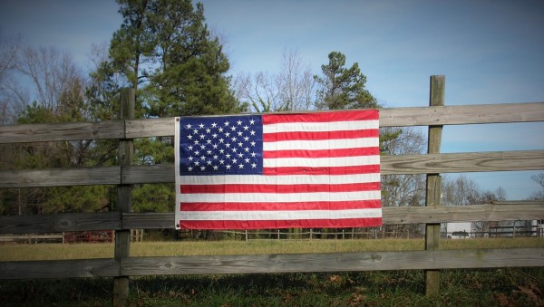 Customer loyalty depicted by the American flag attached to a slatted fence out in a country setting with large pine trees behind it.