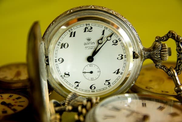 Taking time off before it's too late is illustrated with an antique watch open with the time of 1:08 pm showing. it is upright amidst other antique pocket watches.